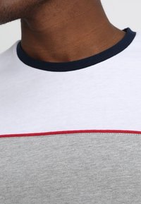 Camiseta de manga corta en gris, blanco y azul marino oscuro con una línea de acento roja, con cuello redondo y textura de algodón suave.