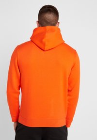 Sudadera naranja brillante con capucha ajustable, puños acanalados y dobladillo. Fabricada con una tela suave y lisa, presenta un diseño trasero sin costuras.