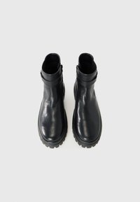 Bottines en cuir noir avec une texture lisse, bout arrondi et semelle épaisse. Présentent une fermeture éclair sur le côté et un design minimaliste.