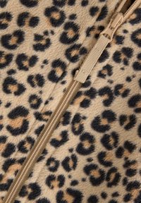 Leopardenmuster-Fleece-Stoff mit beigem Hintergrund, der schwarze und braune Flecken zeigt. Ein beiger Reißverschluss verläuft vertikal entlang einer Seite.