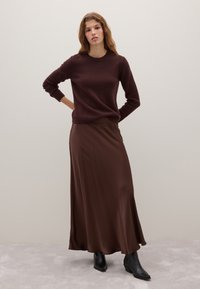 Brauner Strickpullover und langer, fließender brauner Satinrock. Schwarze Ankle Boots mit spitzem Zehenbereich. Einfache, glatte Texturen und einfarbige Farben.