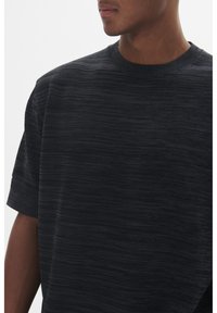 Tricou tricotat închis la culoare, cu un model texturat, decolteu rotund și mâneci scurte. Materialul pare moale și ușor elastic.