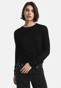 Zwarte, lange mouwen sweater met een ronde hals en strakke manchetten, gecombineerd met zwarte jeans met zilveren knoopaccenten en zakken.