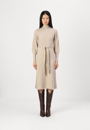 Knit beige dress with ribbed texture, high neckline, and waist tie. Paired with dark brown cowboy boots featuring decorative stitching.