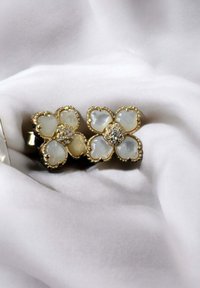 Gold-tone flower-shaped earrings featuring light-colored cabochon stones and a central diamond-like accent, set against white fabric.
