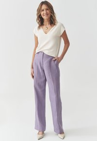 White silky top with scalloped neckline paired with high-waisted lavender wide-leg trousers. Cream pointed-toe shoes.