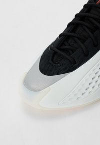 Sort sportssko med tekstureret mesh-overdel, sølvdetalje og gennemsigtig hvid sål med et sekskantet mønster.