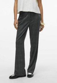 Pantalons à carreaux en tissu noir et gris, avec une taille haute et une coupe large, associés à des chaussures noires et un haut léger.