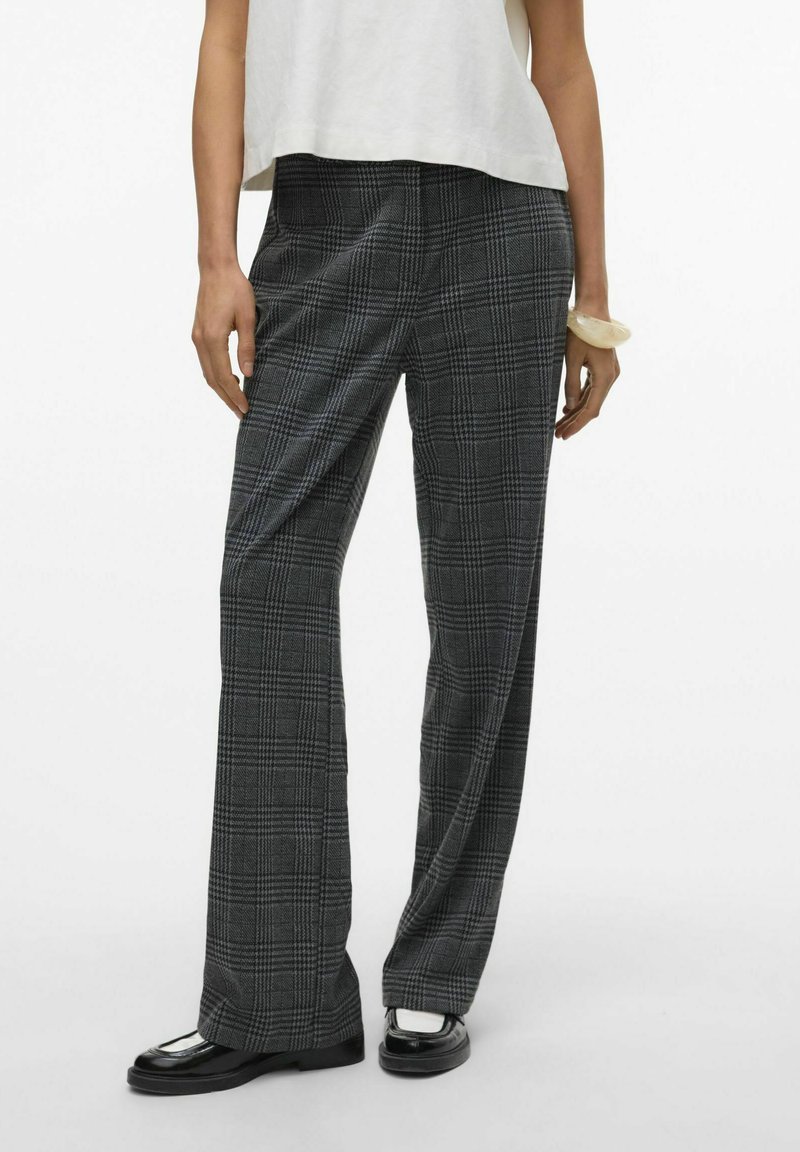 Pantalons à carreaux en tissu noir et gris, avec une taille haute et une coupe large, associés à des chaussures noires et un haut léger.