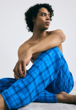Pantalons de lounge à carreaux bleus en tissu doux, présentant un motif à quadrillage de lignes noires, ajustés à la taille et avec des ouvertures de jambe décontractées.