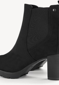 Bottine noire avec panneau latéral élastique, petit talon bloc, et languette à l'arrière, fabriquée en matériau mat semblable au daim.
