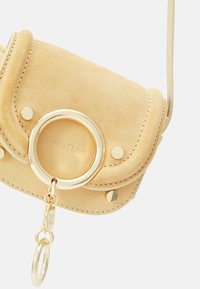 Borsa a tracolla gialla in suede con anello circolare dorato e borchie, con cuciture visibili e un'etichetta di marca all'interno.