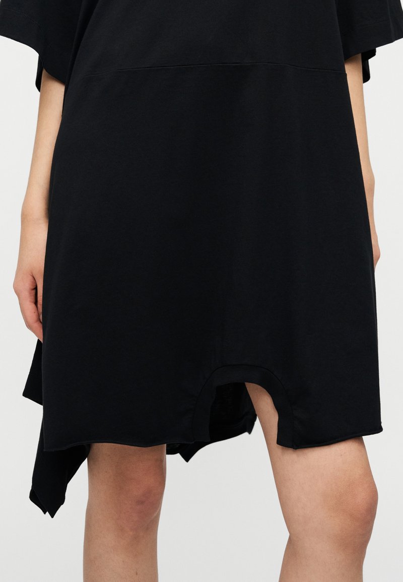 Robe en coton noir avec un ourlet arrondi et une fente latérale. Caractérisée par une coupe ample et des manches courtes. Texture lisse avec un minimum de détails.