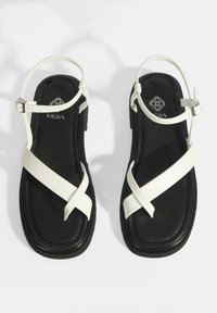 Witte leren bandjes sandalen met zwarte zool, met een kruisontwerp en verstelbare enkelgesp. Gladde afwerking en gevoerde voetbed.