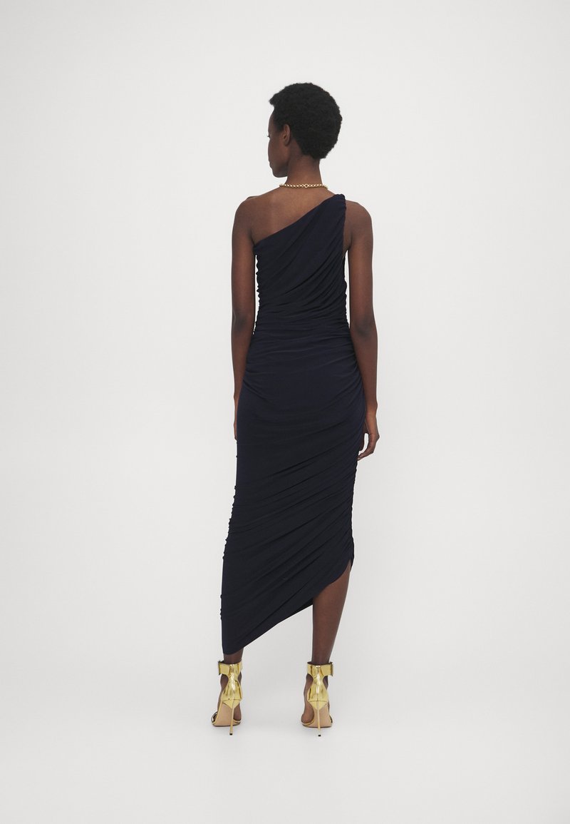 Marineblå én-skulder kjole med sammensamlet tekstur, tætsiddende silhuet, sideslids, og ankelremssandaler med guldfinish.