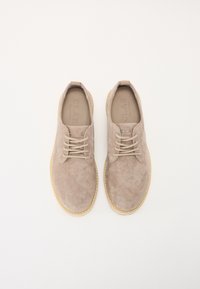 Beige suede shoes with a round toe, lace-up design, and thin light-colored sole. The interior features a textured insole with branding.