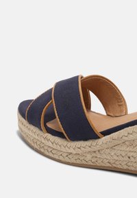 Sandali platform in tela blu navy con dettagli in pelle marrone e suola in giute intrecciato. Presentano due cinturini incrociati per una calzata sicura e confortevole.