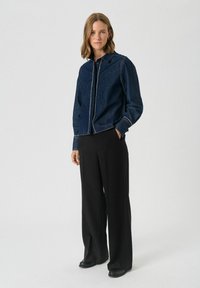 Donkerdenim overhemd met een knoopsluiting aan de voorkant en contrasterende witte stiksels. Gecombineerd met zwarte wijde broek en platte schoenen.
