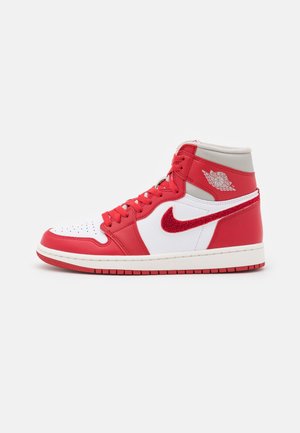Zapatilla alta Air Jordan roja y blanca con cordones rojos, un logo Nike swoosh rojo de ante y un logotipo de alas de Air Jordan en el tobillo.
