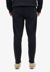 Mørkeblå sweatpants med en afslappet pasform, der har en glat tekstur og elastisk talje. Sammen med beige sneakers.