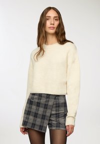 Maglione lavorato a maglia color crema con collo rotondo, abbinato a pantaloni corti a quadri blu navy con design avvolgente e tessuto testurizzato.