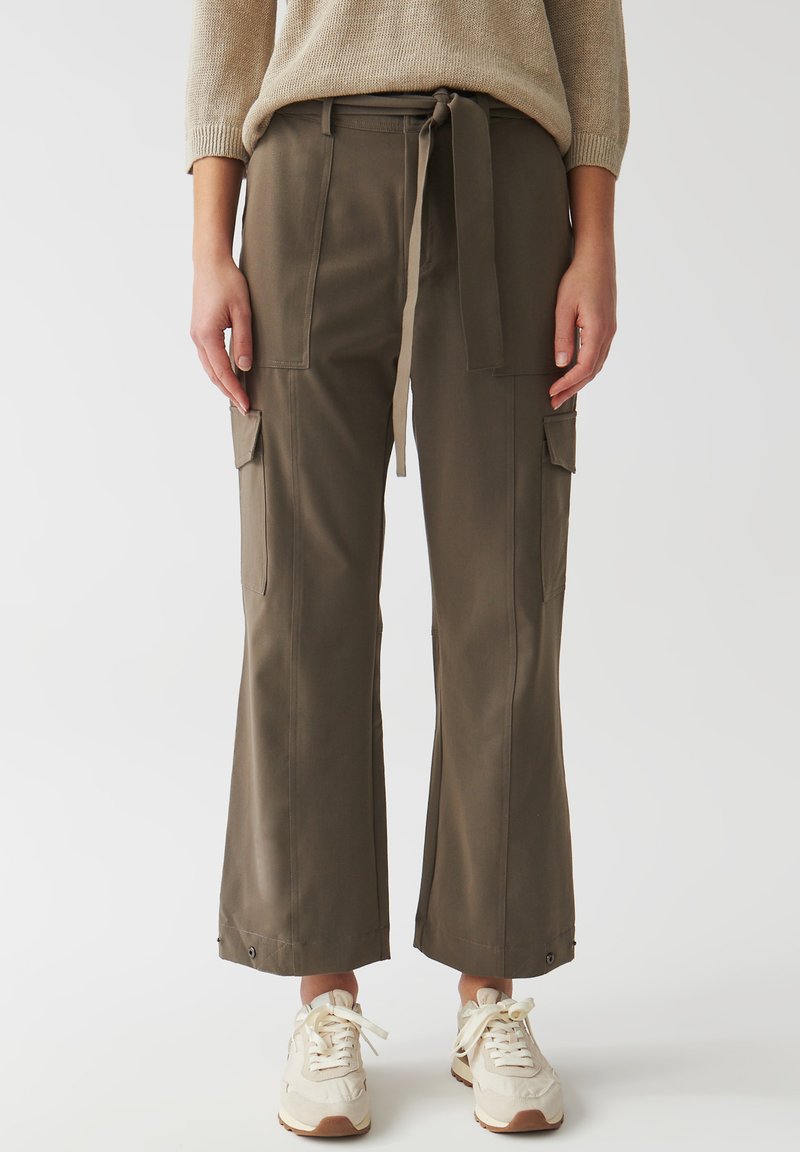 Olivgröna cargobyxor med dragsko i midjan, vida ben och flera fickor. Matchas med beige sneakers. Slät tygtextur.
