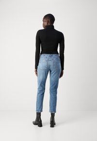 Schwarzes enges Rollkragenhemd, kombiniert mit hellblauen hochgeschnittenen Jeans. Die Jeans haben zwei Gesäßtaschen und eine ausgewaschene Optik. Schwarze Absatzstiefeletten.