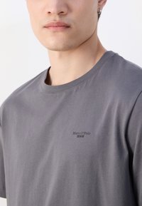 Pelēkas kokvilnas T-krekls ar apaļu kaklu un īsām piedurknēm, ar mazu melnu logo "Marc O'Polo DENIM" uz krūšu daļas.