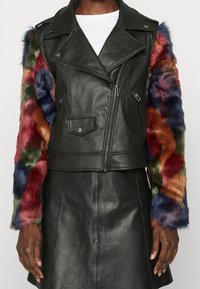 Giacca da biker in pelle nera con maniche in pelliccia ecologica colorata nelle tonalità di rosso, verde, blu e arancione; presenta cerniere e un colletto a risvolto.