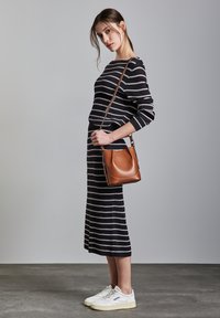 Maglione a righe e gonna midi nei toni blu navy e crema, abbinati a una borsa a tracolla in pelle marrone e sneaker bianche. Design semplice e strutturato.