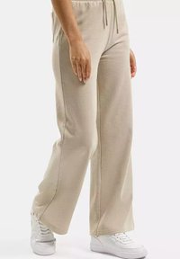 Beżowe dresy o luźnym kroju, z regulowanym ściągaczem w pasie i bocznymi kieszeniami, wykonane z miękkiego materiału o gładkiej teksturze.