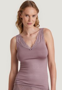 Lichtpaarse mouwloze top met kantafwerking langs de halslijn en een klein strikdetail in het midden, gemaakt van zachte, gladde stof.