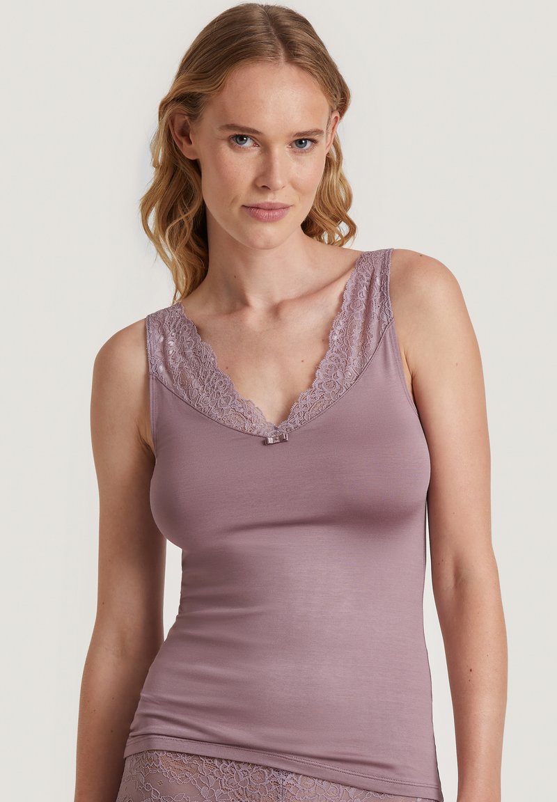 Lichtpaarse mouwloze top met kantafwerking langs de halslijn en een klein strikdetail in het midden, gemaakt van zachte, gladde stof.