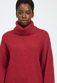Rød turtleneck sweater med en tykk strikketekstur, sænkede skuldre og afslappet pasform. Blødt stof giver et hyggeligt udseende.
