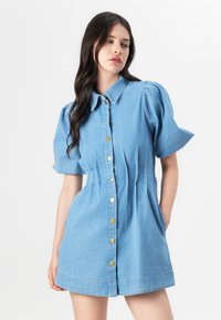 Vestido de ganga azul claro com mangas curtas bufantes, gola tipo camisa e botões dourados à frente. Apresenta bolsos laterais e uma cintura ajustada.