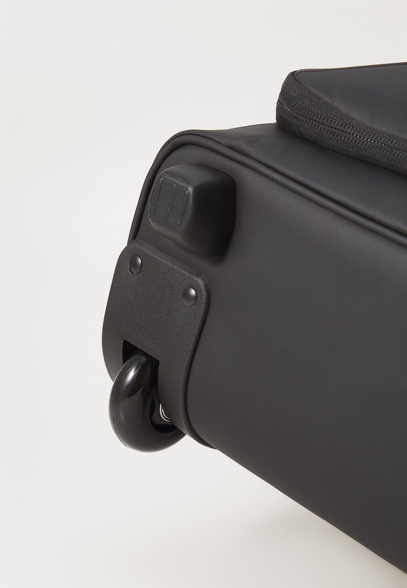 Svart väska på hjul med en slät yta, försedd med ett stabilt handtag och ett runt, glänsande hjul för enkel transport.