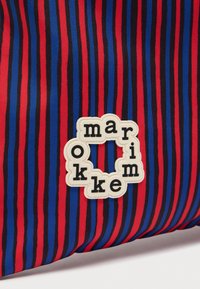 Κόκκινο, μπλε και μαύρο υφασμάτινο με κάθετες ρίγες και ένα λευκό πλαίσιο που φέρει μαύρα γράμματα τοποθετημένα σε κύκλο που σχηματίζουν τη λέξη «marimekko».