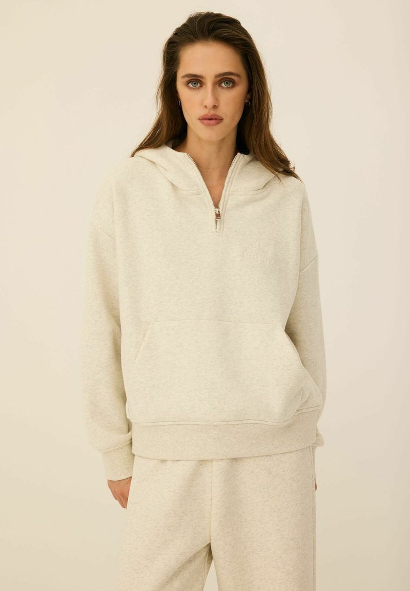 Jasnoszara hoodie na zamek w miękkim materiale z kieszenią typu kangur, prążkowanymi mankietami i kapturem ze sznurkiem. Posiada minimalne detale przeszyć.