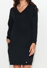 Schwarzes Sweatshirtkleid mit V-Ausschnitt, langen Ärmeln und einem lockeren Schnitt. Verfügt über seitliche Taschen und einen kleinen goldenen Akzent am Saum.