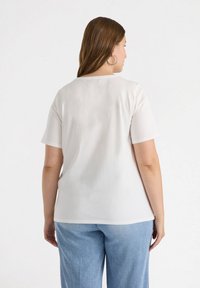 Hvid kortærmet t-shirt med en rund halsudskæring, lavet af et glat stof, set fra ryggen. Sammen med lyseblå denimbukser.