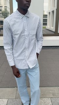 Witte overhemd met lichtblauwe verticale strepen, voorzien van een kraag en een enkele borstzak; gecombineerd met lichtblauwe denim jeans.