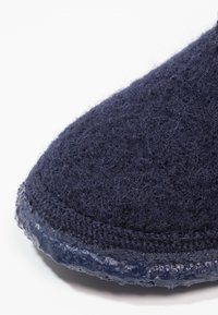 Marineblauwe felt pantoffel met een getextureerde wol bovenkant en een gladde, glanzende rubberen zool, met een ronde neus en gestikte naden.