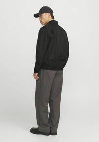 Chaqueta bomber negra con un acabado suave, puños y dobladillo acanalados. Combinada con pantalones grises holgados y calzado negro, presenta una gorra de béisbol.