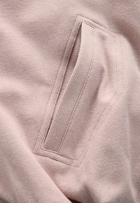 Lichtroze sweatshirtstof met een paspelzak met een gestructureerd oppervlak en verstevigde naden, wat het zachte en gezellige materiaal accentueert.