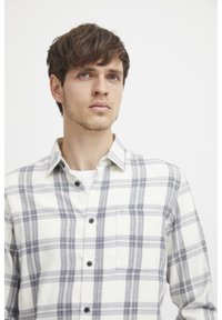 Plaid button-up shirt in white with blue and gray lines. Features a collar, chest pocket, and dark buttons. Cotton material with medium weight texture.