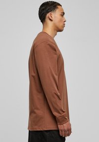 Camisa marrón de manga larga hecha de algodón suave, con un corte holgado, cuello redondo y puños acanalados. Mostrada de lado.