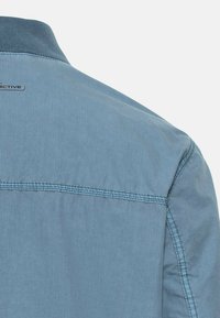 Lichtblauw shirt met een soepele textuur, button-down kraag en gestikte accenten op de rug. Logo vlakbij de kraag.
