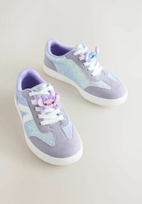 Lilac and glittery sneakers with white soles and laces, decorated with cartoon character charms on the laces, on a light background.