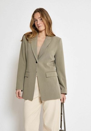 Olive green blazer with a tailored design, notched lapels, front pockets, and single button closure, paired with cream-colored pants.