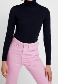 Marinblå polotröja med långa ärmar, tillverkad av mjukt tyg. Matchad med rosa högmidjade jeans med framfickor och silverdetaljer.